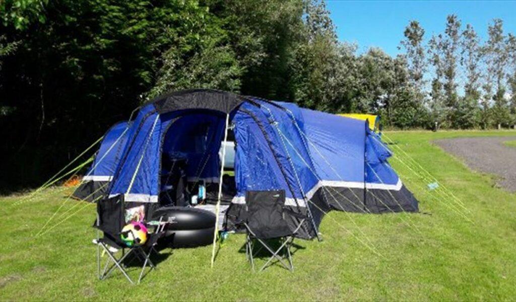 Blue camping tent with chairs set up on a grassy campsite