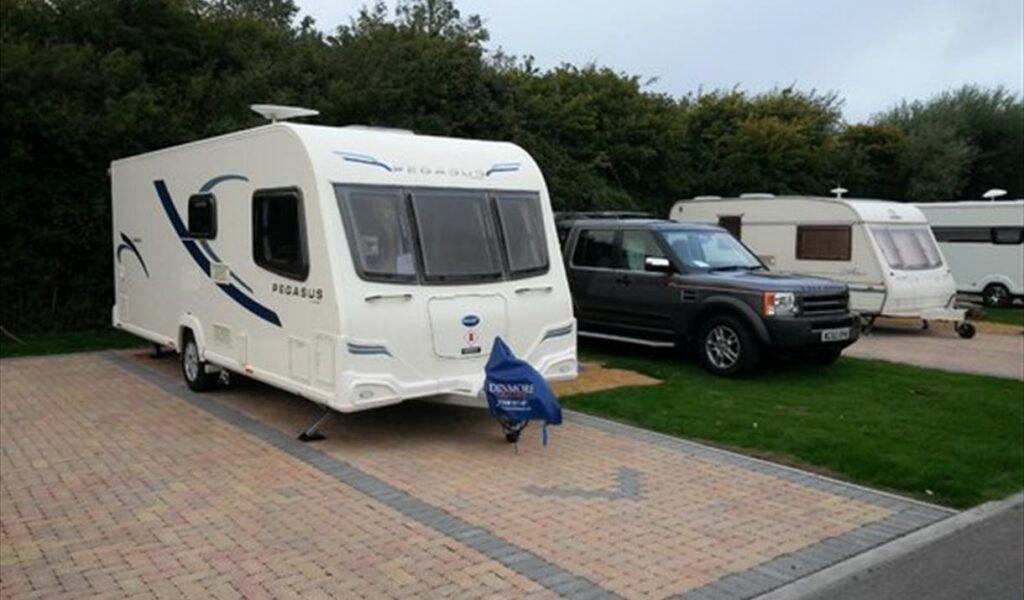 Caravan parked on a campsite next to a black SUV, with other caravans in the background