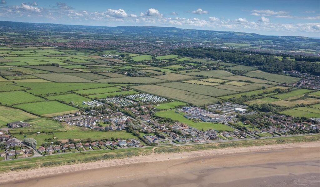 Aerial view of a coastal town beside a sandy beach and patchwork farmland under a blue sky