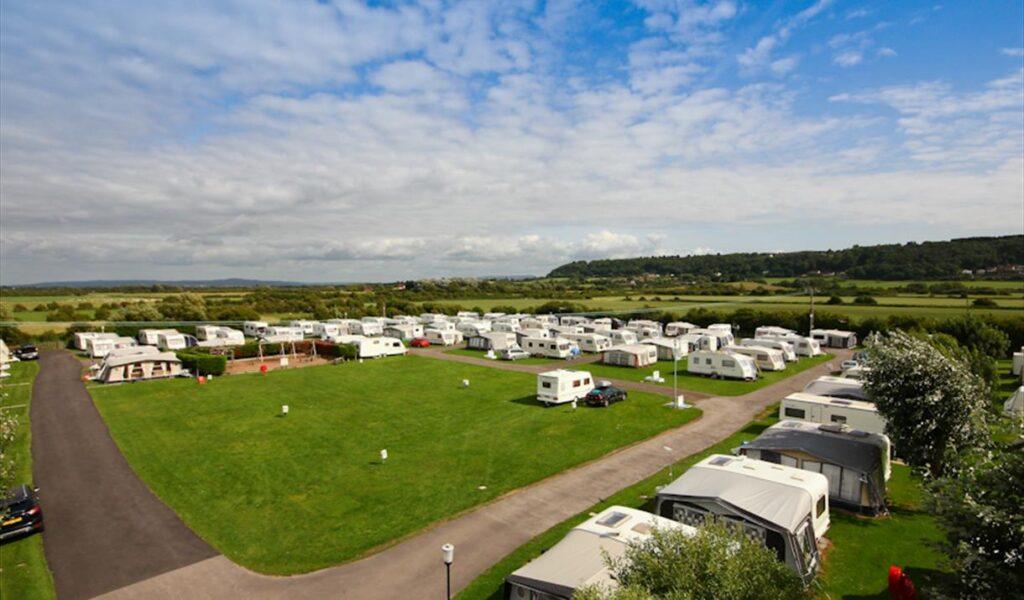 Caravan park with rows of parked campers and trailers on a grassy field under a cloudy sky