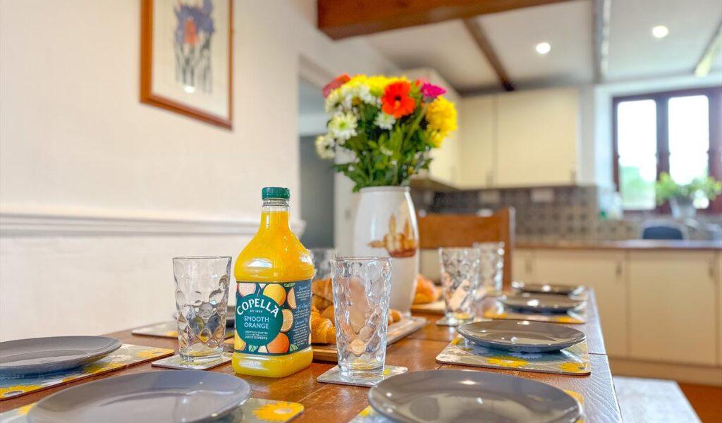Dining table set for a meal with orange juice, glasses, plates, and a vase of flowers