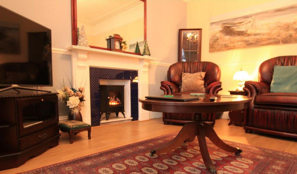 Living room with a fireplace, leather chairs, coffee table, TV, and patterned rug