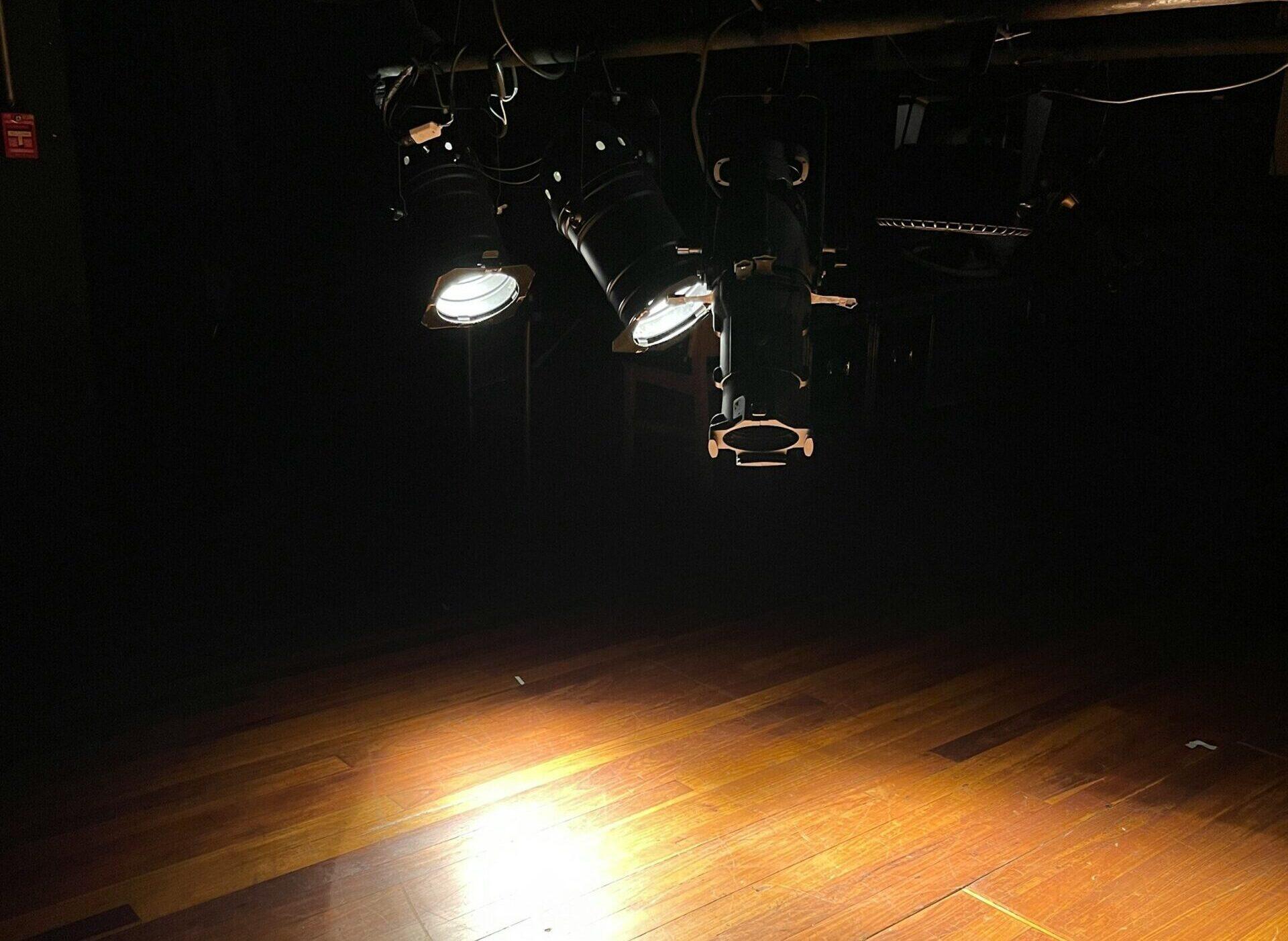 Three spotlights are above a stage, two of them are shining light into the stage.