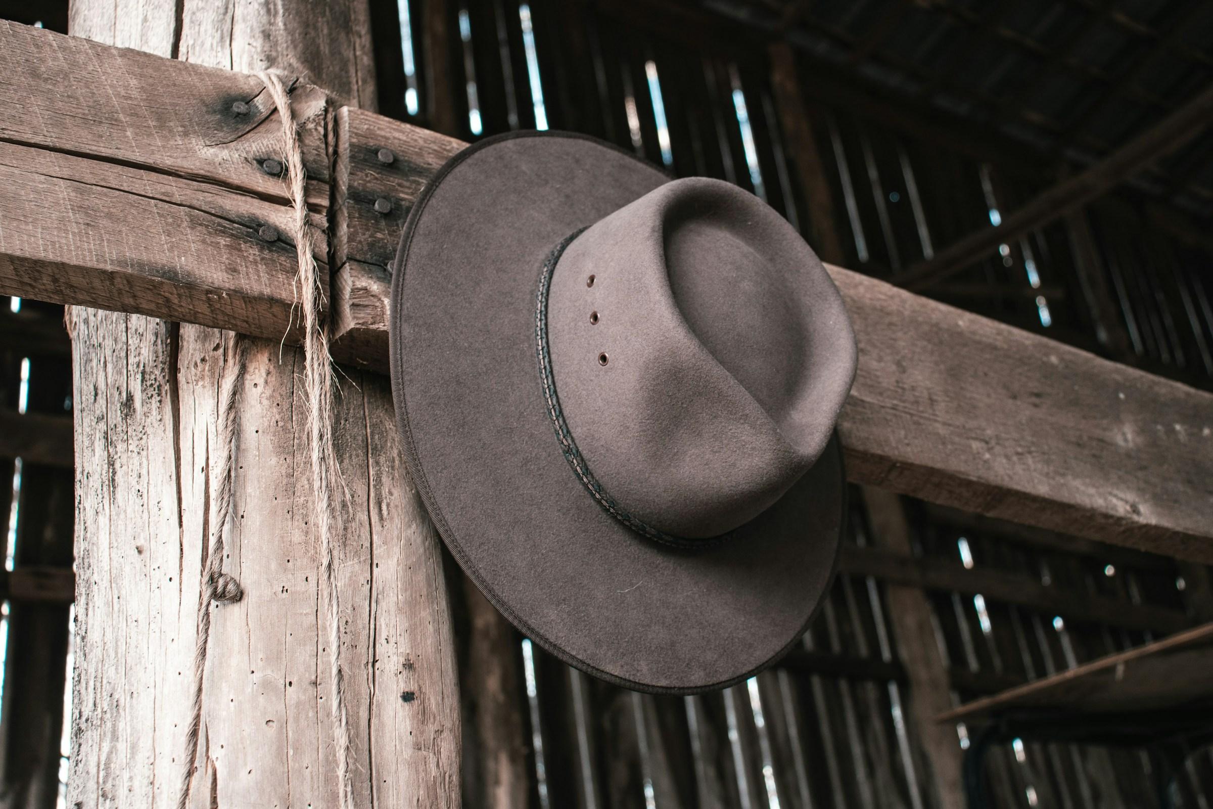 A cowboy hat hangs in a wooden shed.