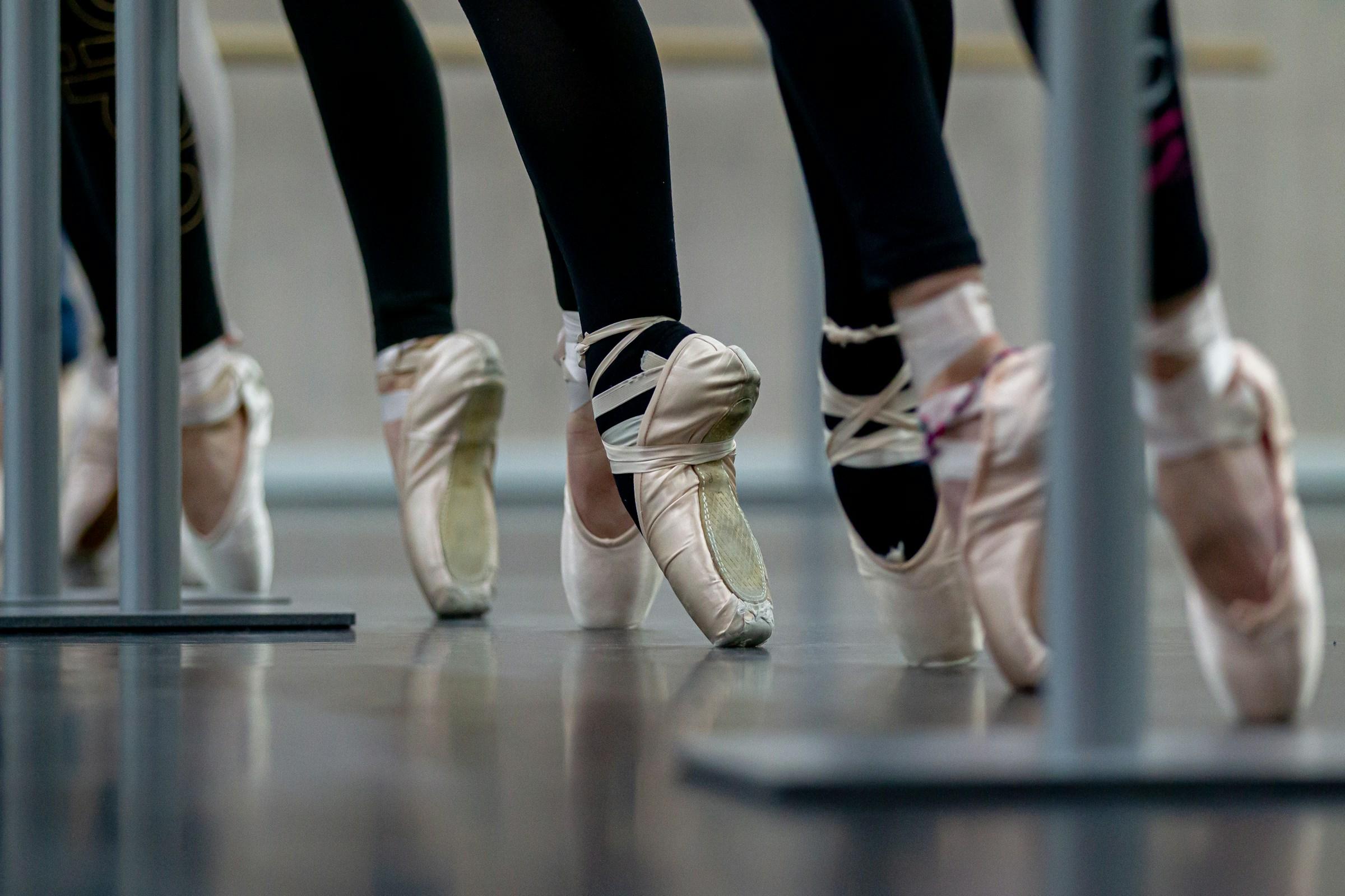 A close up of a line of people wearing ballet shoes, standing on toes.