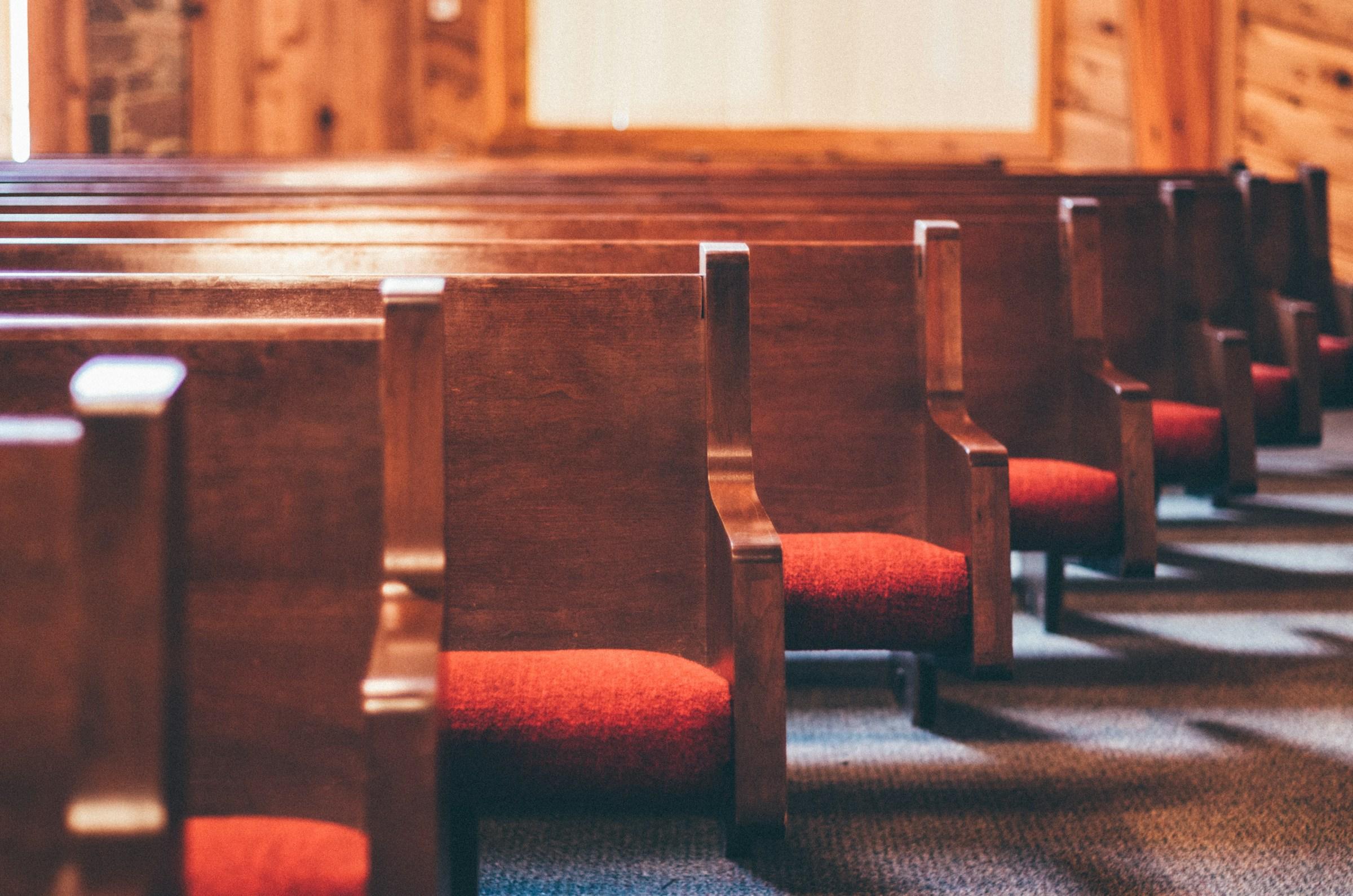 A line of wooden church pews with red seats.