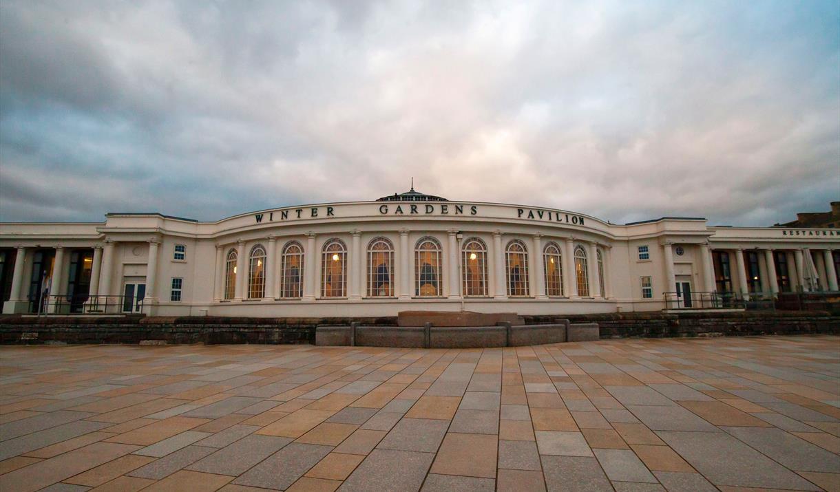 The front of the Winter Gardens Pavilion, with a dramatic grey, blue and pink sky.