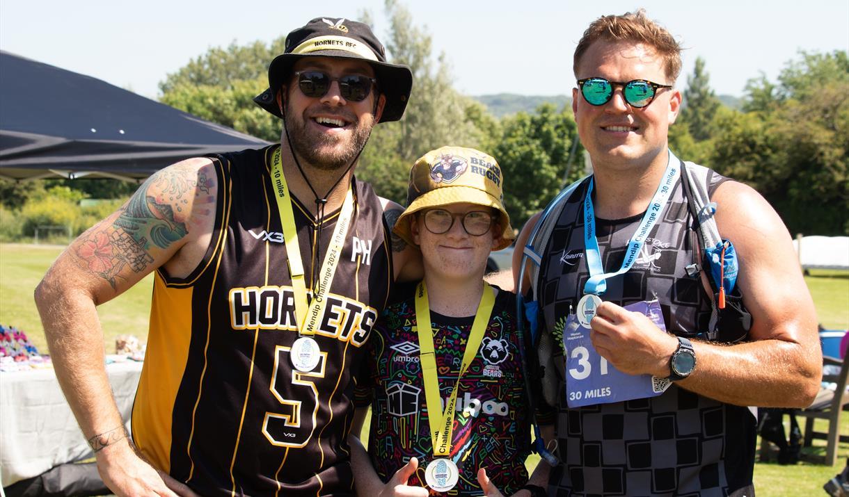 Three people take part in the Mendip Challenge - they are wearing medals and fitness outfits.