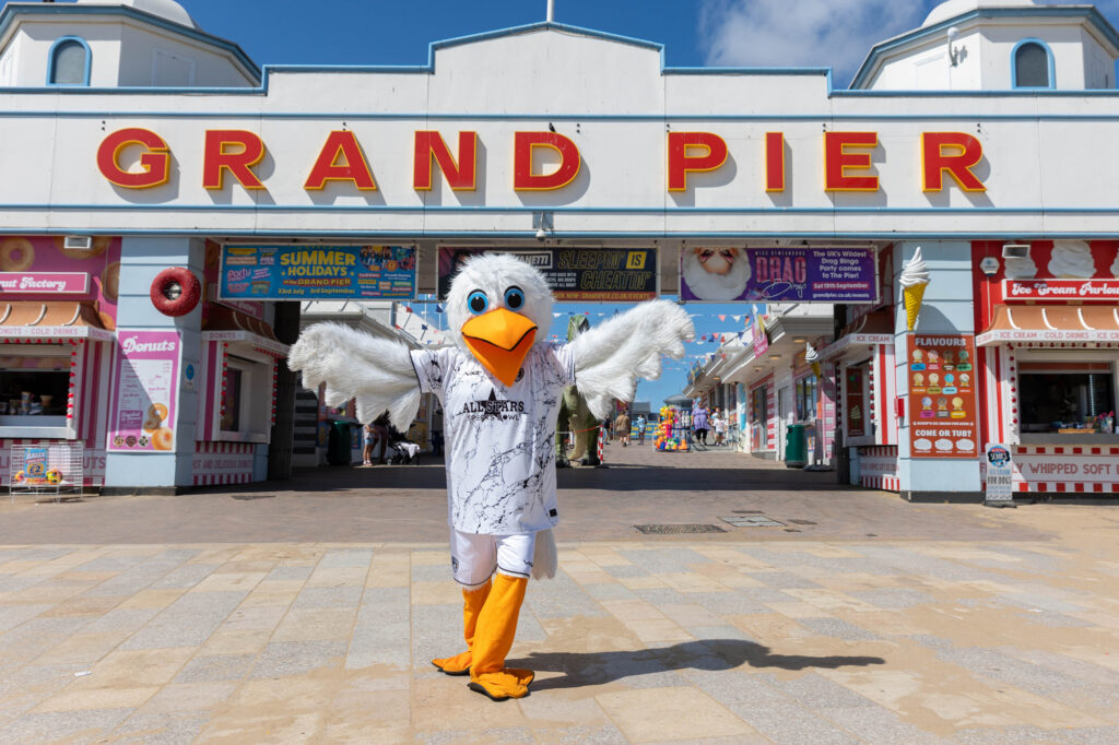 A large seagull mascot flapping its wings under the sign for the Grand Pier in Weston-super-Mare