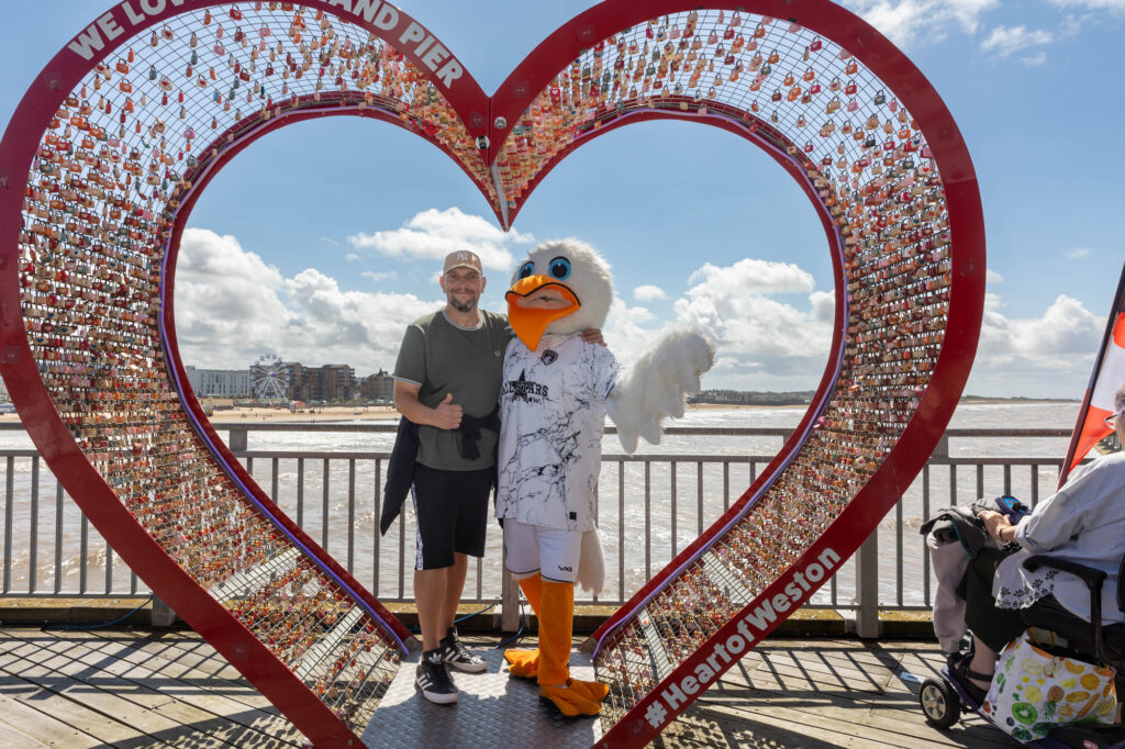 A giant seagull mascot and a man stand together inside a giant red heart-shaped arch