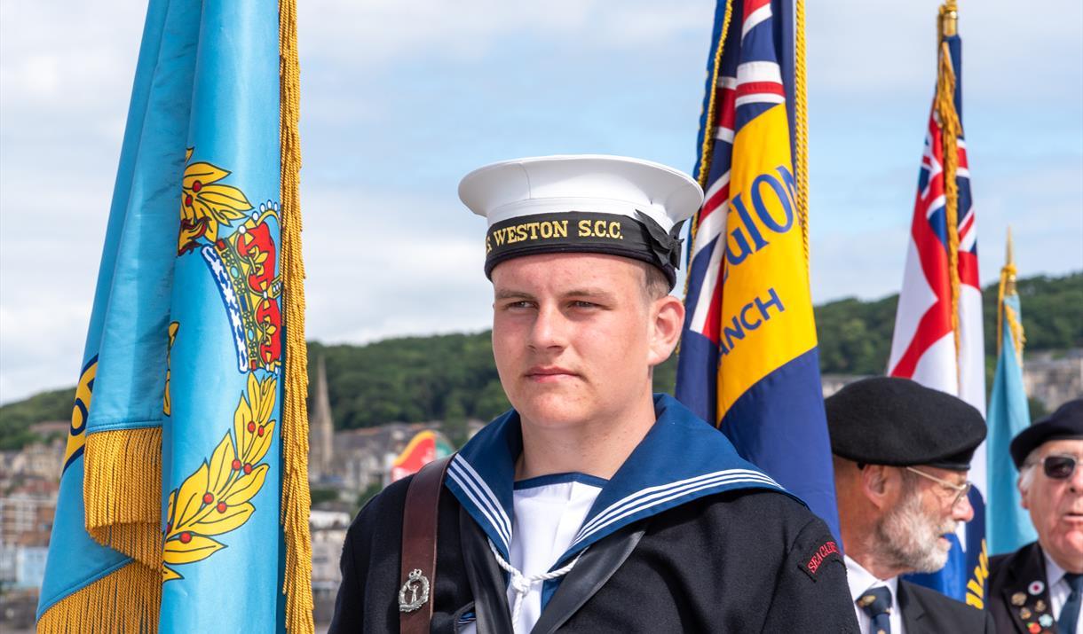 A person in a sea cadet uniform holds a flag at Armed Forces Day.