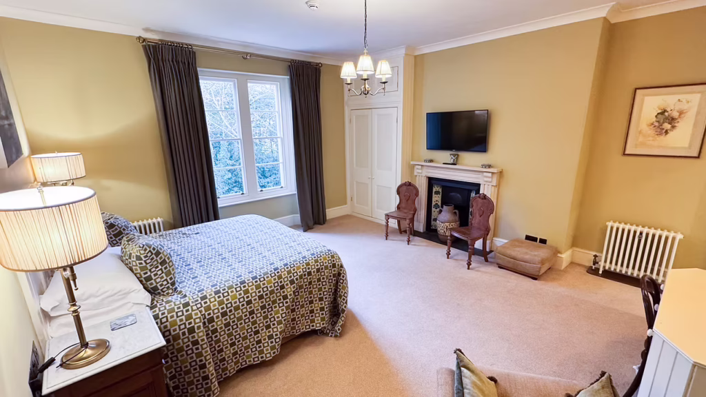 View of a modern double bedroom at Uphill Manor featuring the original fireplace and antique chairs