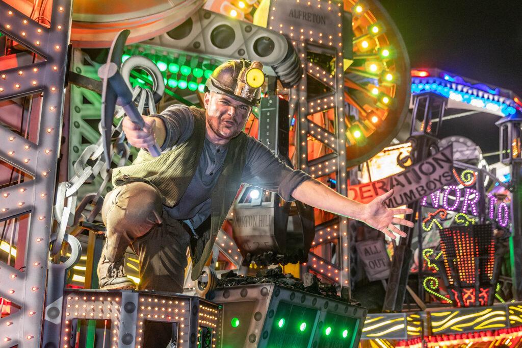 A performer from the Ramblers Carnival float leans forward holding an axe