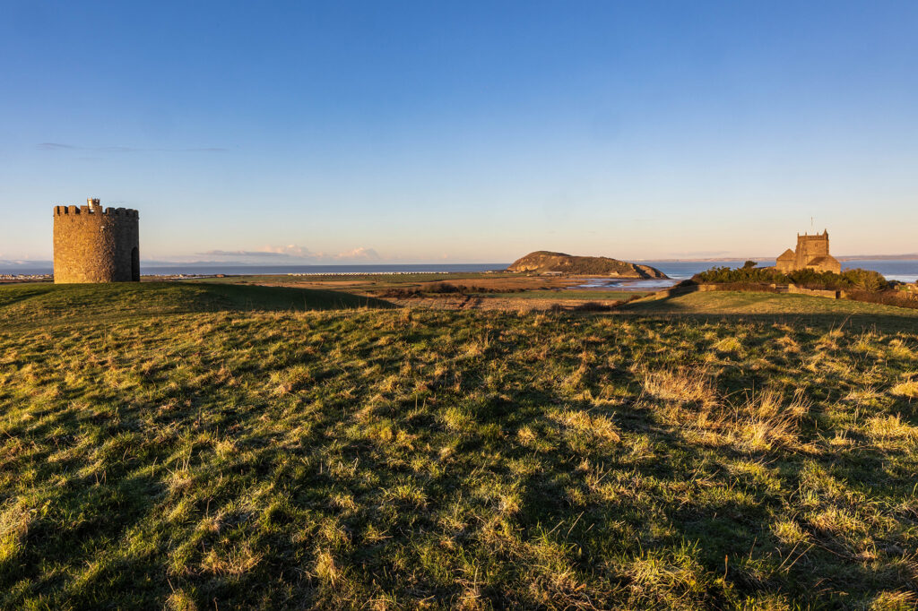 Looking across a sunlit field towards Uphill Church & Beacon with Brean Down and the sea in the background