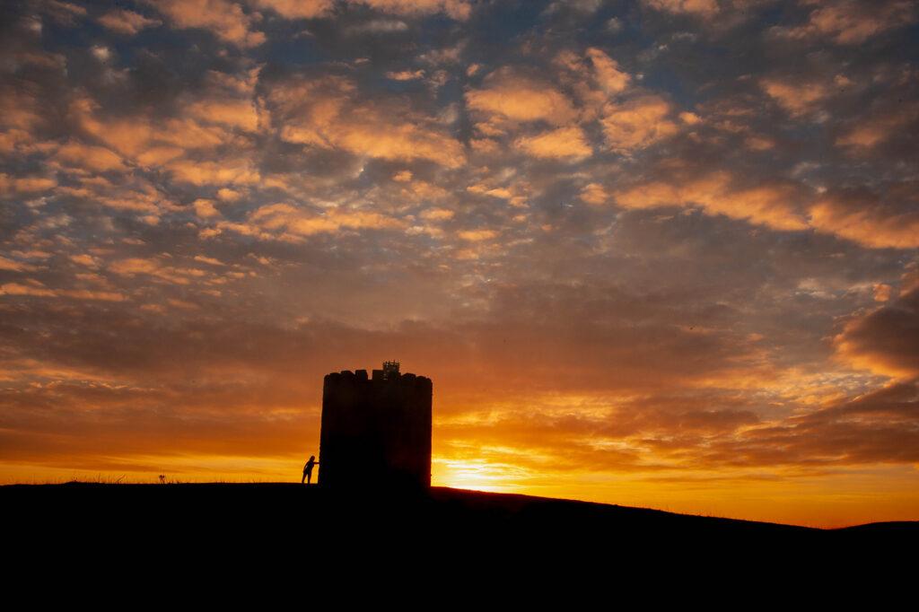 A runner in silhouette takes a rest leaning against Uphill viewing tower at sunrise