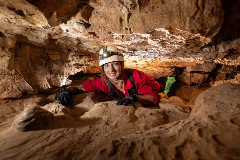 A climber wearing a red boiler suit crawls through a narrow crevice during the Wild Wookey Experience at Wookey Hole, Somerset