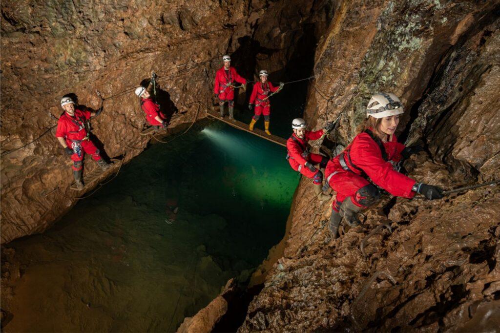 Cavers on the Wild Wookey experience navigate their way past a green underwater pool