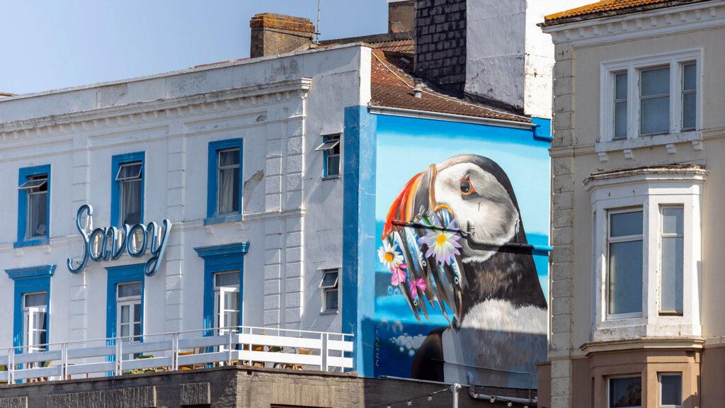 A mural of a puffin with a mouthful of fish on the side of the Savoy Hotel Weston-super-Mare as part of the Weston Wallz Street art programme