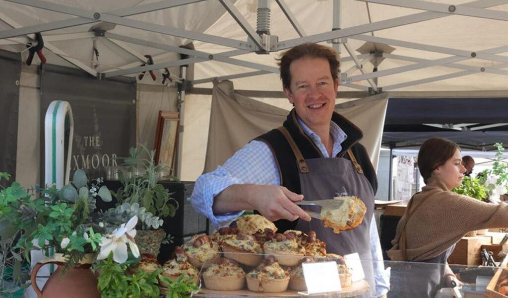 A stall holder at the eat:Weston food festival reaches over the counter to serve a customer a pie