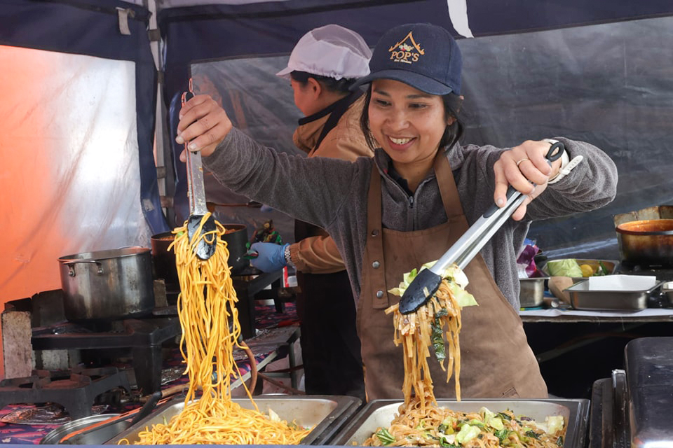 A lady at the eat:Weston food festival holding up some noodles in some tongs and some cooked vegetables in the other set of tongs