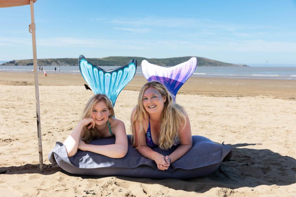 Two women dressed as mermaids lying on the beach at Weston-super-Mare in Somerset