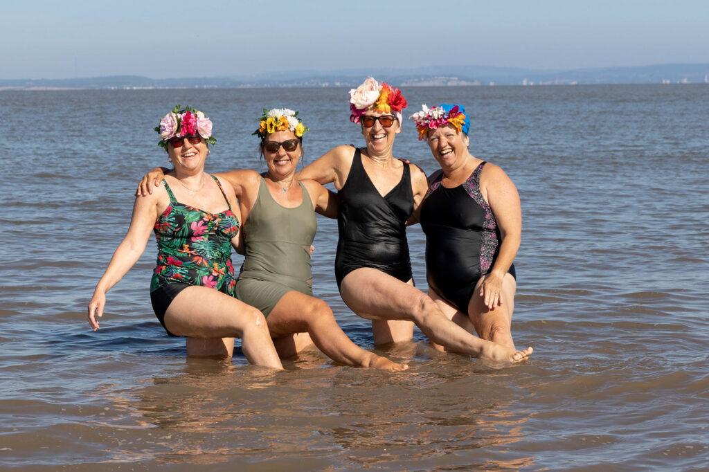 Four lady Swimmers pose for the camera while standing in the sea at Weston-super-Mare