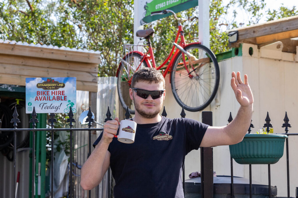 A male worker at the Strawberry Line Cycle Hire project waves at someone while having his coffee break