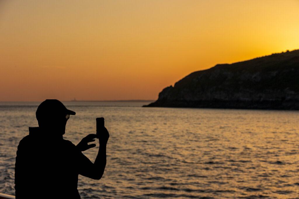 A man on board the Waverley paddle steamer takes a picture of the sunset on his mobile phone