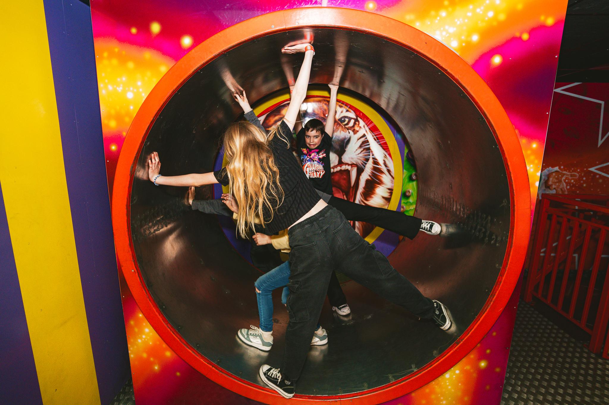 Children with their hands and legs outstretched inside a cylinder as part of the Crazy Circus attraction at the Grand Pier, Weston-super-Mare