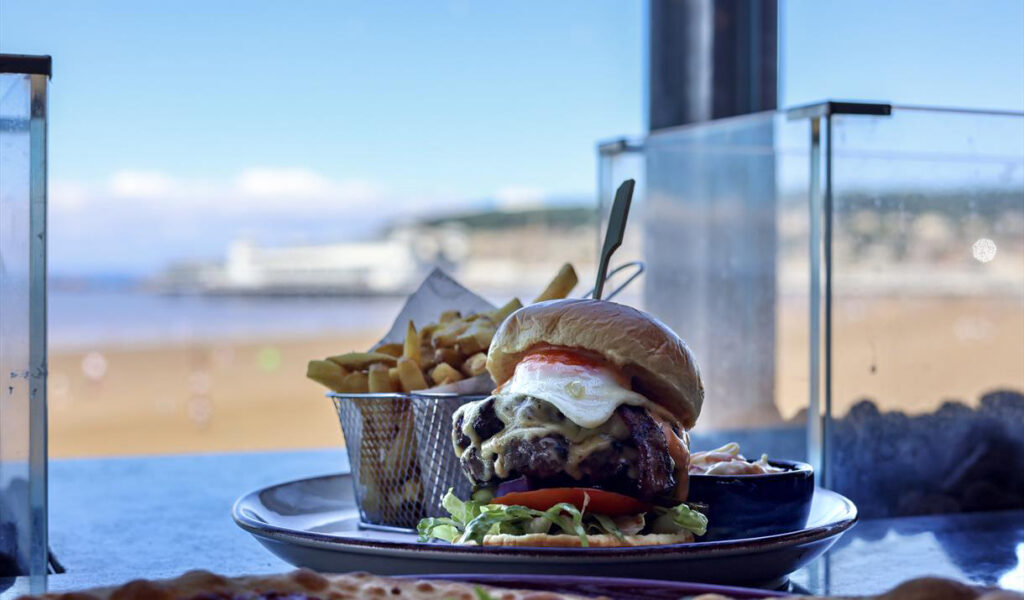 Plate of burger and chips at Revo Pier with the view of Weston through the window