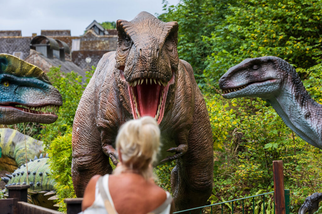 A lady is confronted by three dinosaurs at Dinosaur Valley at Wookey Hole