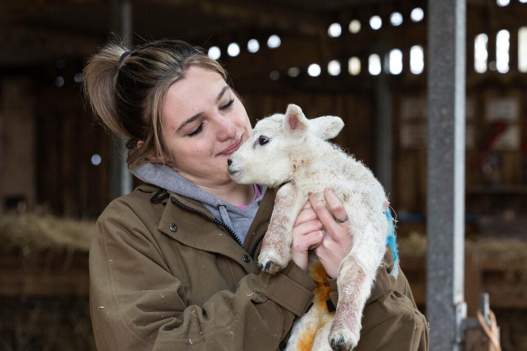 A lady farmer looking down at the baby lamb she's holding in her arms at Court Farm animal attraction near Weston-super-Mare