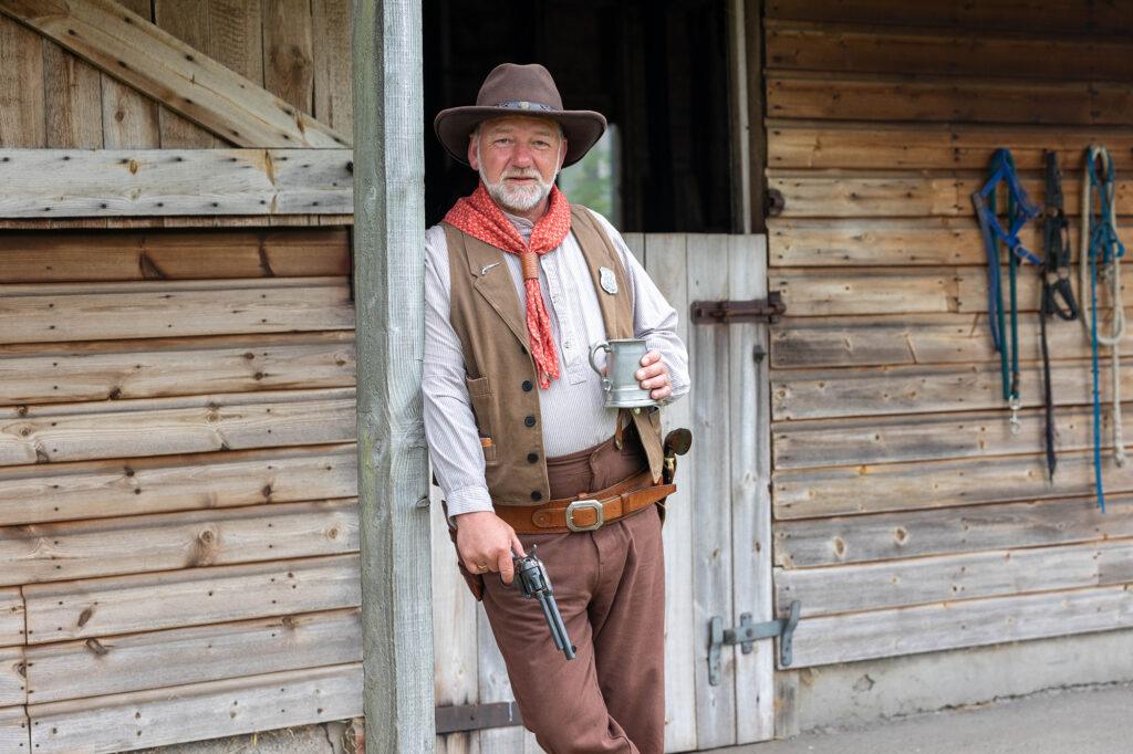 A cowboy with a gun leans against a wooden stable door during a Country & Western Festival at Court Farm, near Weston-super-Mare