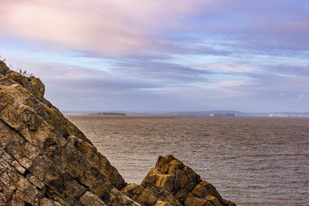 Looking through jagged rocks at the end of Brean Down towards the the island of Flat Holm and the Welsh coast