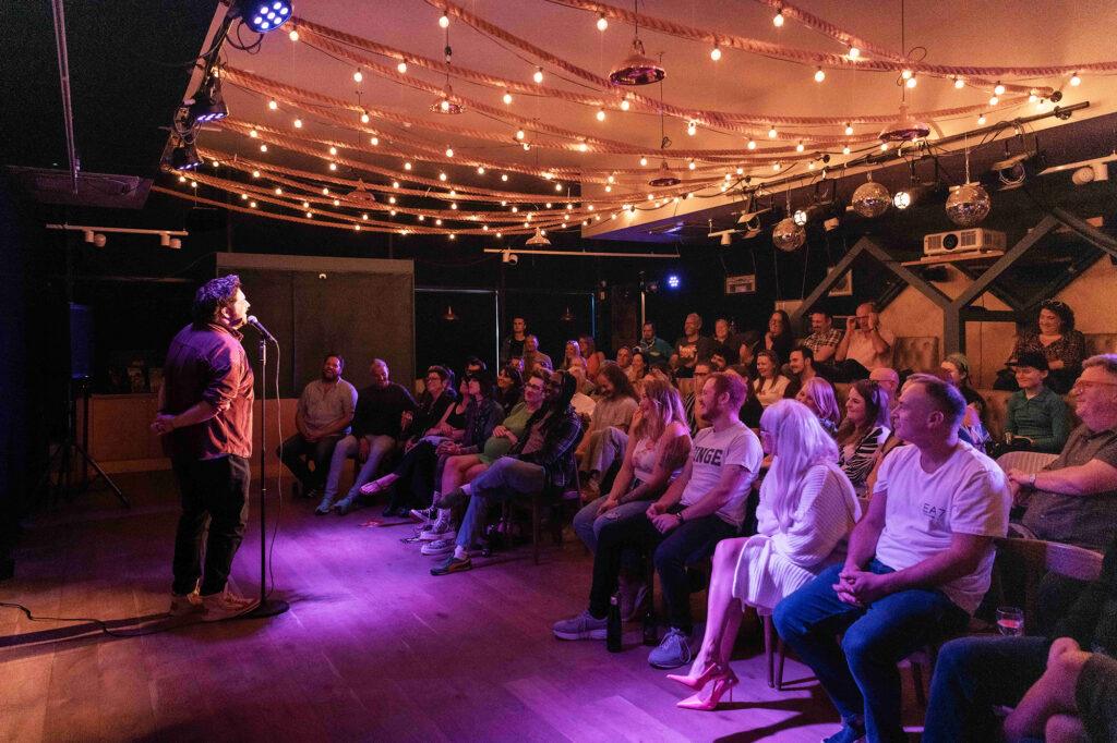 A comedian on stage in front of an audience at The Front Room Theatre, Weston-super-Mare
