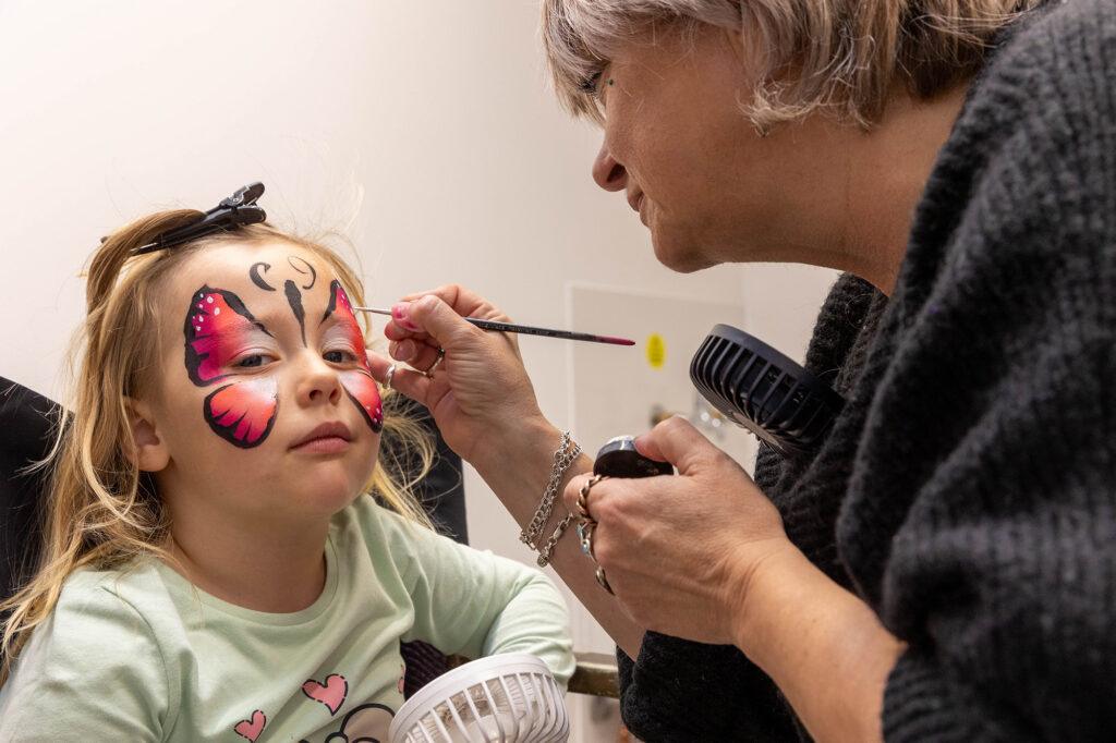 A lady applies face paint in the design of a butterfly on a young girl's face at the Old Town Quarry, Weston-super-Mare