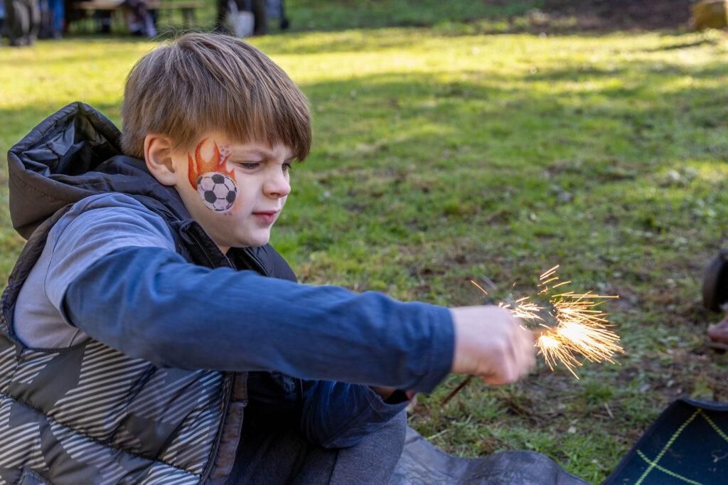 A boy with face paint on his cheek creates a spark by rubbing flint together at the Old Town Quarry, Weston-super-Mare