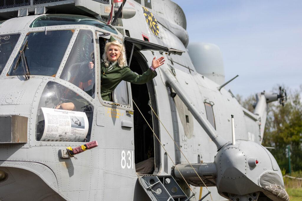 A lady in an army uniform waves out of the window from the pilot's seat of a helicopter at the Weston-super-Mare Helicopter Museum