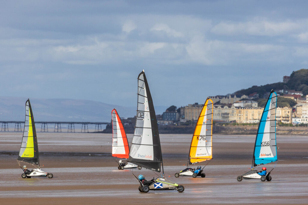 Five Blokart racers in their three wheeled sail carts racing across the sand at Weston-super-Mare Beach