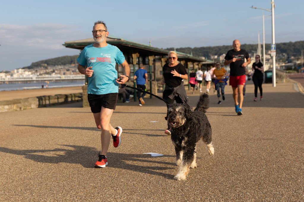 A man and a dog lead a crowd of runners taking part in parkrun in Weston-super-Mare