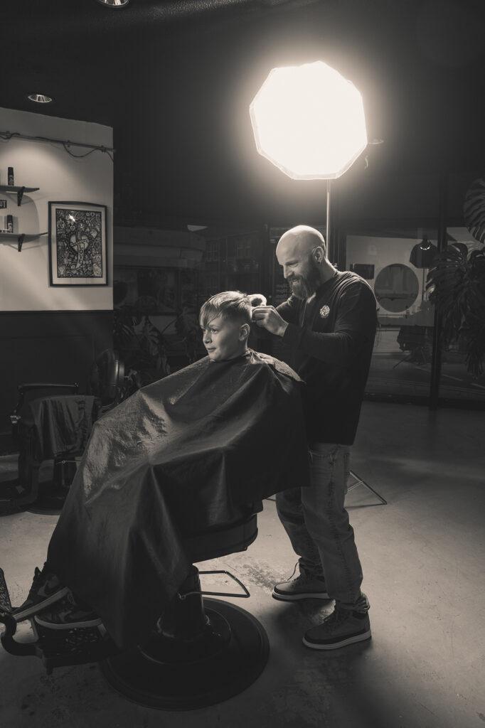 Black and white image of a boy having his hair cut in a barbershop