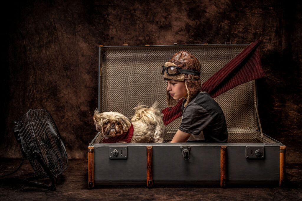 A boy wearing a hat with goggles sitting in a suitcase