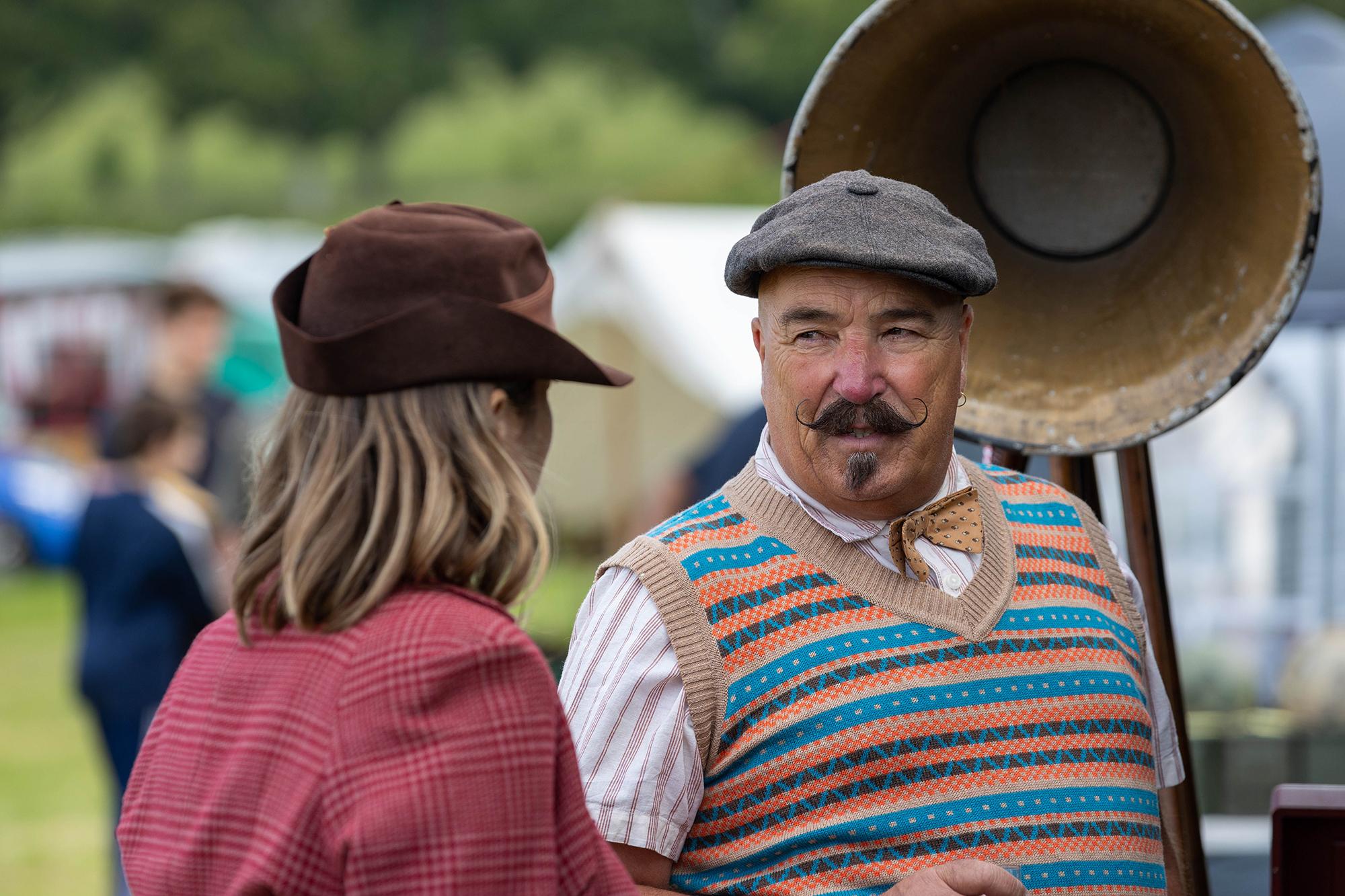 A man with handlebar moustache and wearing 1940's clothes chats to a lady at the Dig for Victory Show in North Somerset