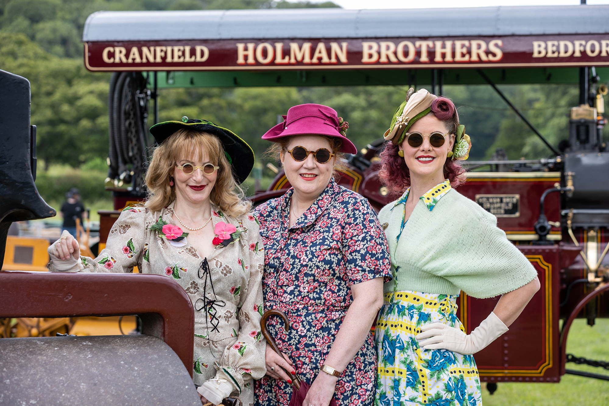 Three ladies in 1940s dress and sunglasses in front of a traction engine at the Dig for Victory Show in North Somerset