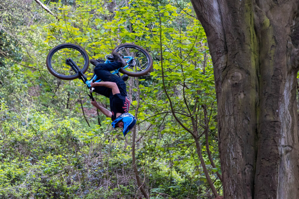 A cyclo-cross rider and his bike fly upside down through the air while taking on the Sand Bay Dirt Jumps in Weston Woods, Weston-super-Mare.