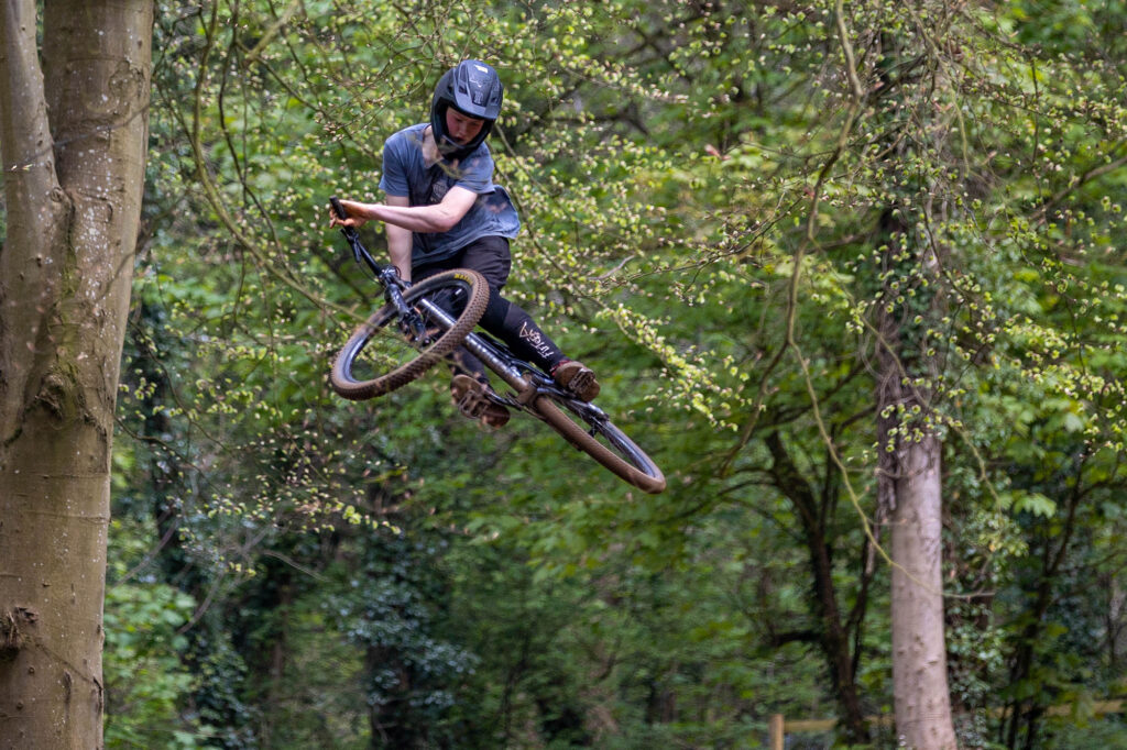 A cyclo-cross rider jumps high into the trees with his bike while taking on the Sand Bay Dirt Jumps in Weston Woods, Weston-super-Mare.