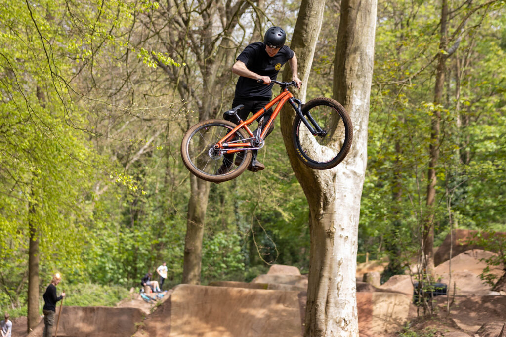 An airborne cyclo-cross rider standing up on one side of his bike while taking on the Sand Bay Dirt Jumps in Weston Woods, Weston-super-Mare.