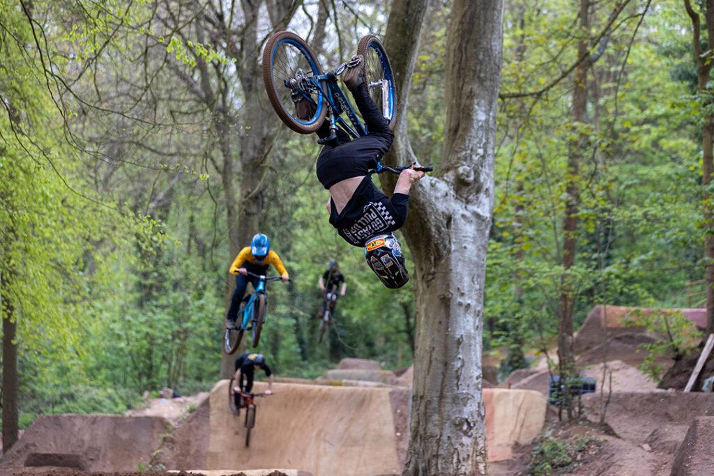 Four cyclo-cross riders taking on the Sand Bay Dirt Jumps in Weston Woods, Weston-super-Mare. The first of the four is upside down in the air as he takes on a 360 move.