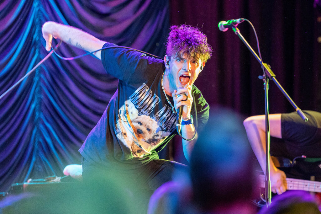 A male singer leans into the crowd and microphone during a concert