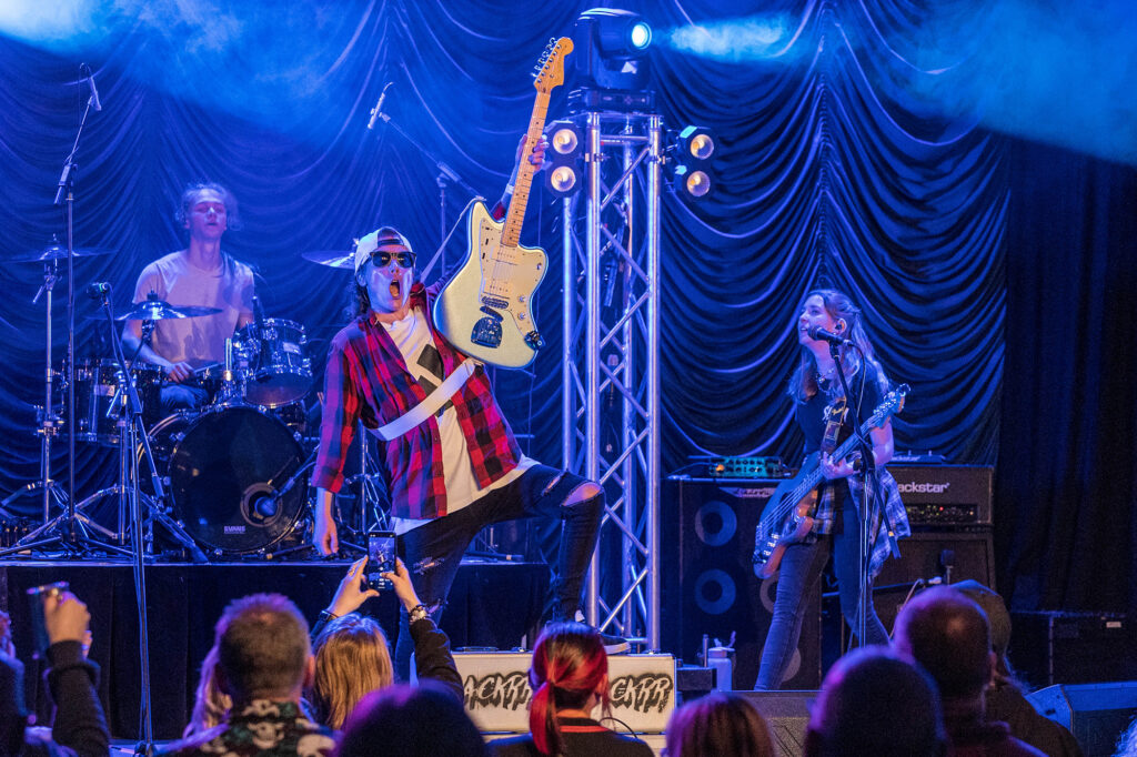 A guitarist holds his guitar aloft and has one foot on the speaker box as he takes the applause of the crowd